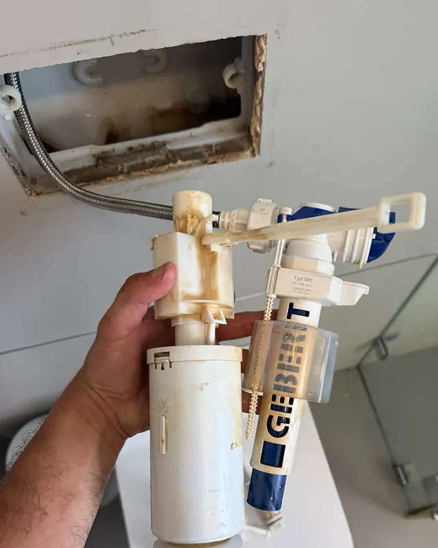 יד מחזיקה מנגנון מילוי ישן ומלוכלך שהוצא מניאגרה סמויה, ומאחור פתח השירות בקיר