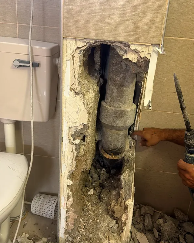 פתח צר וארוך בקיר ליד מיכל ההדחה, ובתוכו צינור הביוב האנכי חשוף. שאר הקיר מחופה אריחים