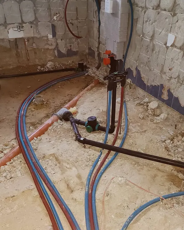 צינורות מים חדשים, כחולים ואדומים, פרוסים על רצפת חדר פתוחה