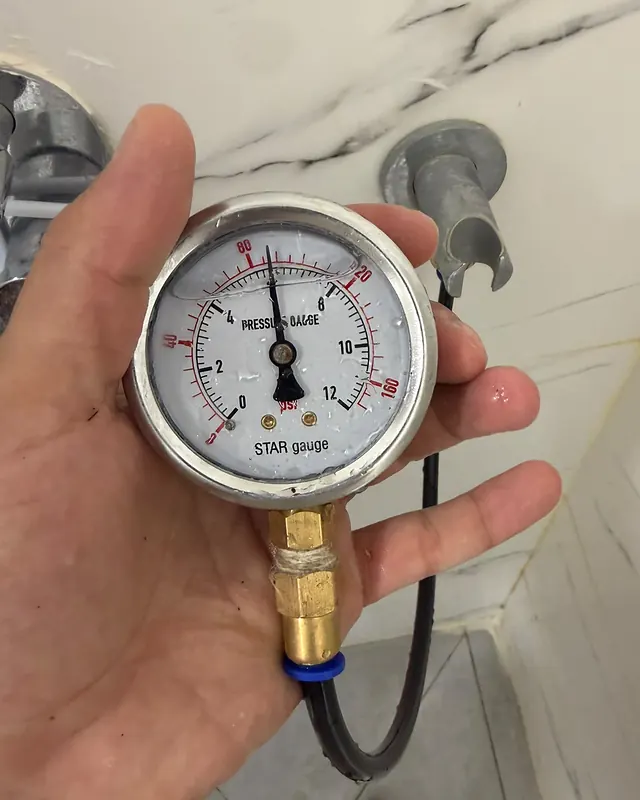 יד מחזיקה מד לחץ עם צינור מחובר, בתוך חדר רחצה
